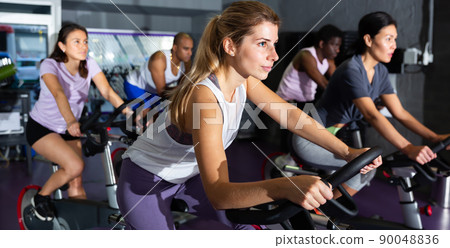 Female cycling on exercise bikes at fitness club 90048836