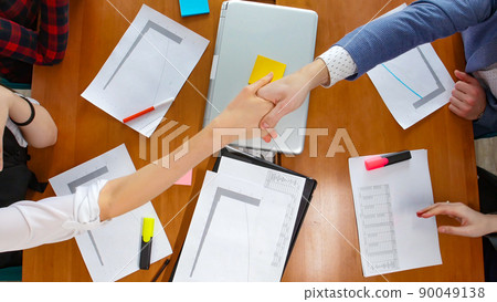 Business concept. People by table greeting each other with a handshake across the table Business concept. People by table greeting each other with a handshake across the table 90049138