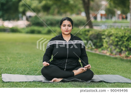 Indian woman doing yoga and meditation in lotus asana pose in outdoor summer park. 90049496