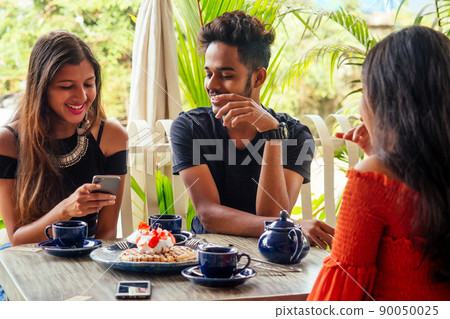 three indian beat Friends eating Sweets pancakes with masala tea in summer tropical beach cafe 90050025