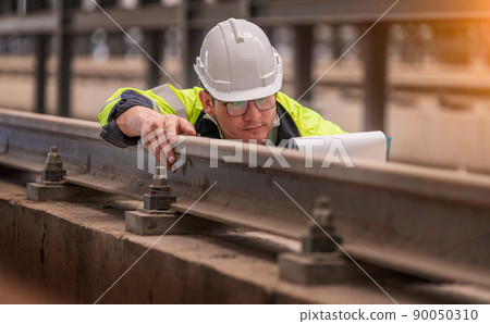 Engineer railway under checking construction process train testing and checking railway work on railroad station with radio communication .Engineer wearing safety uniform and safety helmet in work. Engineer railway under checking construction process train testing and checking railway work on railroad station with radio communication .Engineer wearing safety uniform and safety helmet in work. 90050310
