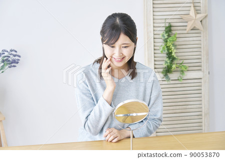A woman who smiles in the living room and looks at her face in the table mirror A woman who smiles in the living room and looks at her face in the table mirror 90053870