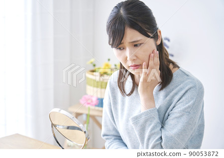 A woman who is worried about looking at her face in the mirror in the living room A woman who is worried about looking at her face in the mirror in the living room 90053872