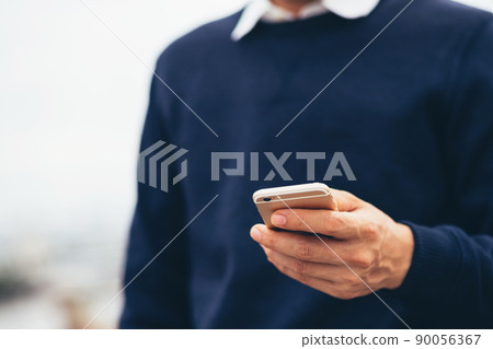 Young man wear plaid shirt.  close up hand using on cell phone during rest on sofa. sitting in watching message on mobile smart phone during break relax. soft focus. 90056367