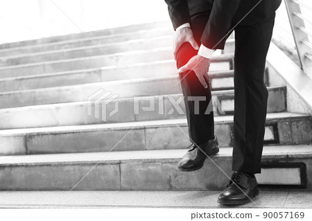 Businessman in a suit have the sore pain and painful knee problem expression and walk up and down on the stairway during go to office. Health care concept. 90057169