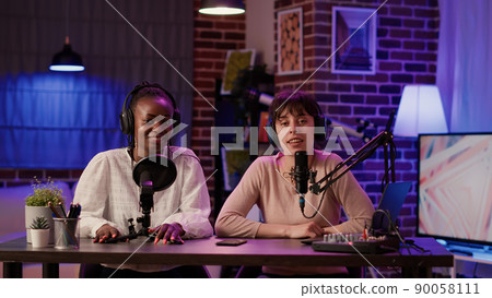 Two women recording dual vlog having casual conversation using professional microphone and audio mixer. Online podcast host talking with african american influencer creating digital content. 90058111
