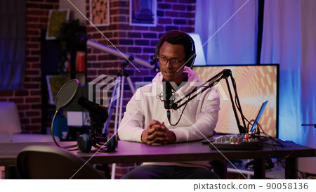 Portrait of african american podcaster adjusting digital audio mixer while talking live to audience using microphone. Male online radio host smiling confident at camera while recording in home studio. Portrait of african american podcaster adjusting digital audio mixer while talking live to audience using microphone. Male online radio host smiling confident at camera while recording in home studio. 90058136