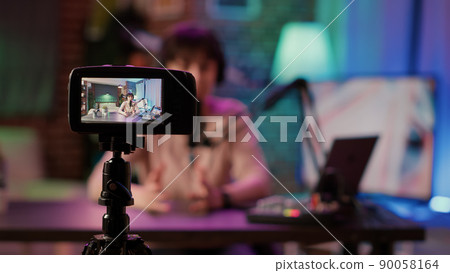 Selective focus on digital video camera screen recording content creator streaming live internet radio using microphone from home studio. Influencer caucasian woman filming vlog for social media post. Selective focus on digital video camera screen recording content creator streaming live internet radio using microphone from home studio. Influencer caucasian woman filming vlog for social media post. 90058164