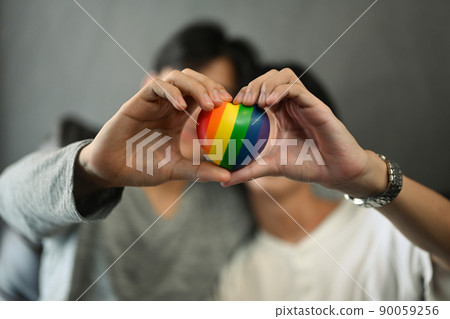 Rainbow heart shape in homosexual couple hands. LGBT, pride, relationships and equality concept Rainbow heart shape in homosexual couple hands. LGBT, pride, relationships and equality concept 90059256
