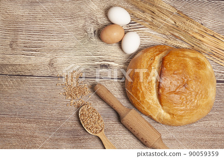 Loaf of round bread with egg, wheat ears, grains, rolling pin on a wooden table top view. Culinary background, baking concept 90059359