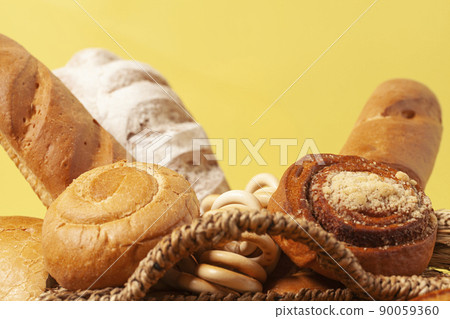 Culinary background with bread,buns,drying bagels,wheat ears in a wicker basket, on yellow. 90059360