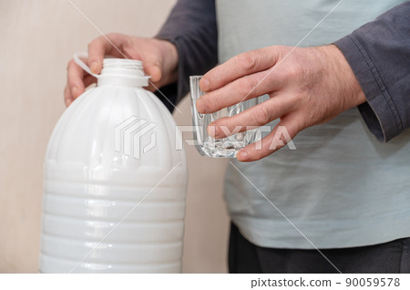 A man is holding an empty glass in his hand. An open white plastic bottle in the background. 90059578