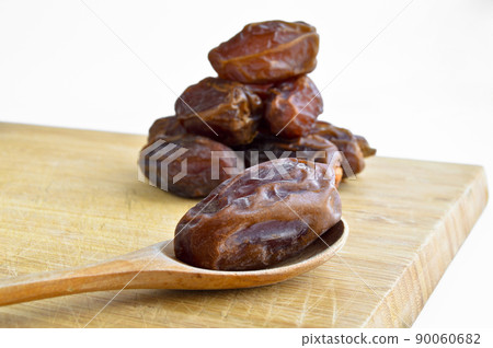 Organic dried hurma dates medjool grains, in wooden spoon on cutting board Organic dried hurma dates medjool grains, in wooden spoon on cutting board 90060682