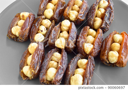 Dried hurma dates medjool grains, hazelnuts placed inside the date, in a gray plate Dried hurma dates medjool grains, hazelnuts placed inside the date, in a gray plate 90060697