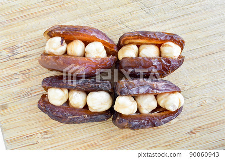Dried hurma dates medjool grains, hazelnuts placed inside the date, on the cutting board 90060943