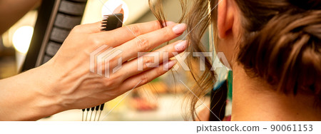 Professional hairdresser styling and fixing with hairspray long woman curly hair in a beauty salon Professional hairdresser styling and fixing with hairspray long woman curly hair in a beauty salon 90061153