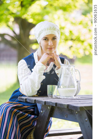 Latvian woman in traditional clothing with milk glass on nature Latvian woman in traditional clothing with milk glass on nature 90061635