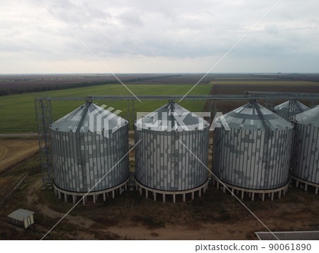 Grain elevator. Metal grain elevator in agricultural zone. Agriculture storage for harvest. Grain elevators on green nature background. Exterior of agricultural factory. Nobody. Grain elevator. Metal grain elevator in agricultural zone. Agriculture storage for harvest. Grain elevators on green nature background. Exterior of agricultural factory. Nobody. 90061890
