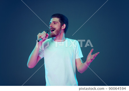 Handsome man in white t-shirt singing at microphone isolated on dark blue studio background, Concept of human emotions, facial expression, sales, ad, fashion and beauty 90064594