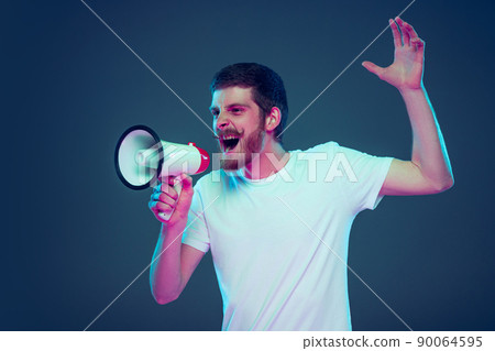 Guy shouting at megaphone. Handsome caucasian man's portrait isolated on dark blue studio background. 90064595