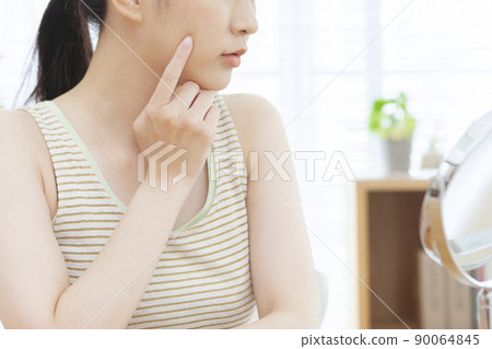 A woman looking at her face in the mirror 90064845