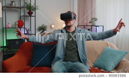 Adult man use virtual reality headset glasses at home, enjoying video concept moving hands in air 90065986
