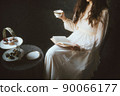 A woman in a dress reading while drinking tea 90066177