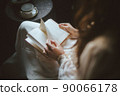 A woman in a dress reading while drinking tea 90066178