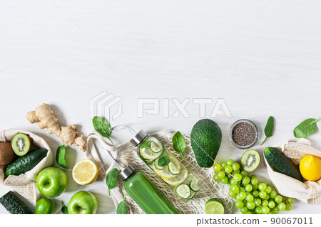 Composition of green fruits and vegetables with bottles of smoothie and infused water on white wooden table top view. Detox diet. 90067011