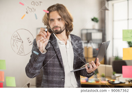 Male employee using laptop and writing on glass board indoor Male employee using laptop and writing on glass board indoor 90067362