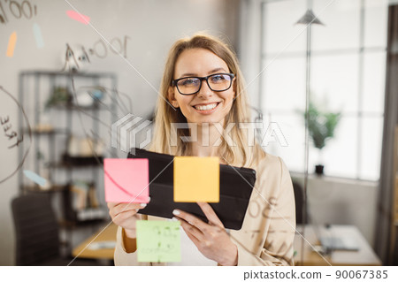 Female office worker with tablet standing near glass board Female office worker with tablet standing near glass board 90067385