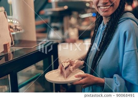 Plate with piece of cheesecake in hands of female smiled waitress in cafeteria. Pastry shop. Plate with piece of cheesecake in hands of female smiled waitress in cafeteria. Pastry shop. 90068491