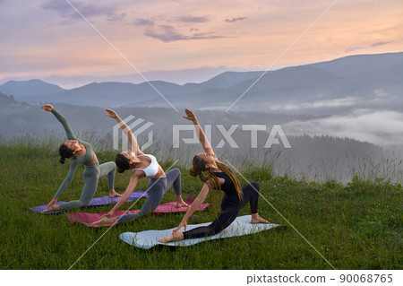 Sporty young women in activewear doing yoga exercises among green mountains. Athletic females stretching body on yoga mat during summer sunset. Sporty young women in activewear doing yoga exercises among green mountains. Athletic females stretching body on yoga mat during summer sunset. 90068765