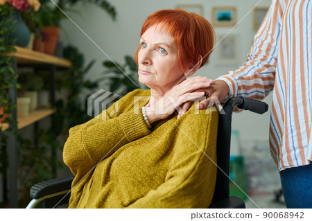 Close-up of African caregiver putting hand on shoulder of senior woman in wheelchair, she supporting her at home 90068942