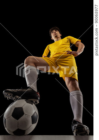 Bottom view of young professional football, soccer player standing with ball isolated on dark background. Concept of sport, match, active lifestyle, goal and hobby Bottom view of young professional football, soccer player standing with ball isolated on dark background. Concept of sport, match, active lifestyle, goal and hobby 90068977