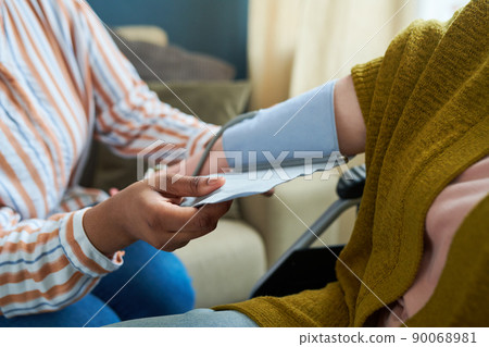 Close-up of nurse checking blood pressure of senior patient during visit to home 90068981