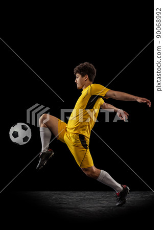 Dynamic portrait of professional football, soccer player training with ball isolated on dark background. Concept of sport, match, active lifestyle, goal and hobby 90068992