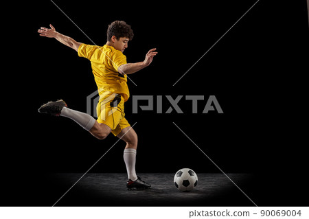 Dynamic portrait of professional football, soccer player training with ball isolated on dark background. Concept of sport, match, active lifestyle, goal and hobby 90069004