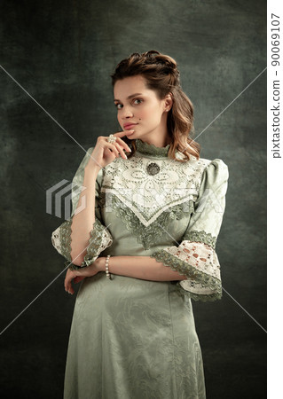 Vintage portrait of young beautiful girl in gray dress of medieval style isolated on dark background. Comparison of eras concept, flemish style. Art, beauty 90069107