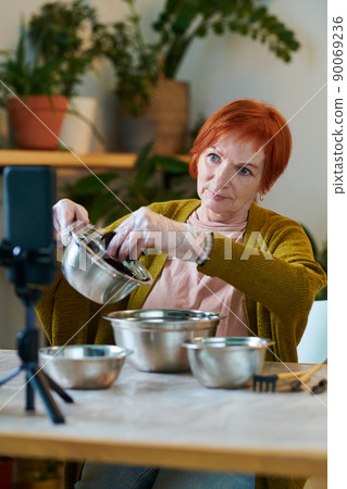 Mature woman using her mobile phone for streaming, she sitting at table and telling about planting Mature woman using her mobile phone for streaming, she sitting at table and telling about planting 90069236