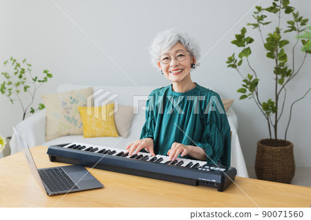 Gray-haired woman playing the keyboard in the living room 90071560