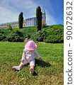 Little girl sitting on green grass turning her head back on wood background 90072632