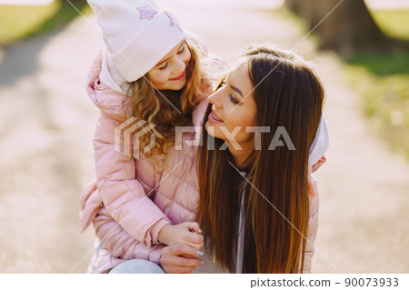 Family in a summer park. Mother in a pink jacket. Little girl walks in a park. 90073933