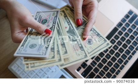Woman hands holding dollar bills earned by working from laptop at home on Internet Woman hands holding dollar bills earned by working from laptop at home on Internet 90074016