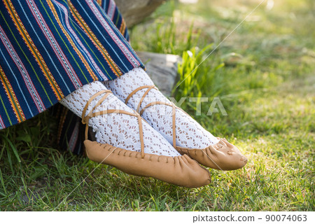 Leather bast shoes of a Latvian woman in traditional clothing. Preparing Ligo festival. Riga. Latvia Leather bast shoes of a Latvian woman in traditional clothing. Preparing Ligo festival. Riga. Latvia 90074063