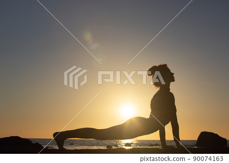 woman practicing stretching at sunset. seaside background, silhouette woman practicing stretching at sunset. seaside background, silhouette 90074163