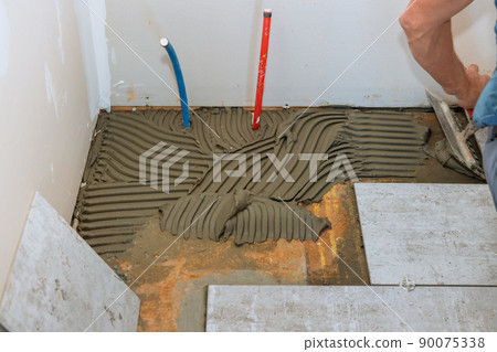 Applying tile adhesive to the floor for floor tile installation witht tiler 90075338