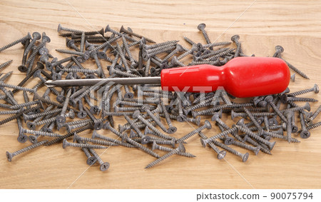 A pile of old screws and a screwdriver closeup to the background of the tree A pile of old screws and a screwdriver closeup to the background of the tree 90075794