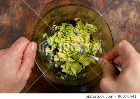Man's hands mashing several avocados in a bowl with a fork to prepare a rich and fresh guacamole. Healthy food concept. Man's hands mashing several avocados in a bowl with a fork to prepare a rich and fresh guacamole. Healthy food concept. 90076441