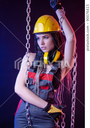 a construction girl in a hard hat and overalls with a long chain in her hands a construction girl in a hard hat and overalls with a long chain in her hands 90076815